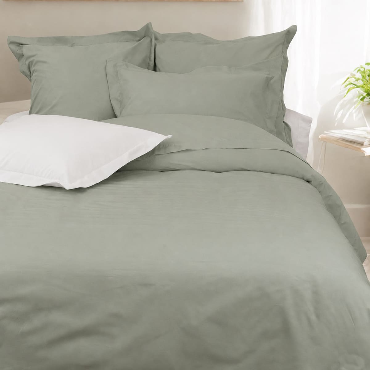 Parure coton percale 200 fils haut de gamme, coloris vert sauge dans une chambre épurée, un oreiller blanc posé sur le lit pour contrasté
